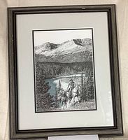 Framed black and white print featuring two riders on horses in prairie scene with mountains and river in background.