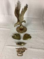 Full lot showing vintage brass eagle, two heart trinket trays, shoe ashtray, and flagpole topper on white background