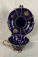 Top and side angle of cup and saucer showing deep cobalt blue color, gold floral decoration and scalloped edges.
