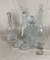Overview of all five glass liquor decanters with two extra stoppers positioned on surface, showing various shapes and styles.