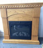 Front view of oak fireplace surround with electric fireplace insert showing natural wood finish and glass front.