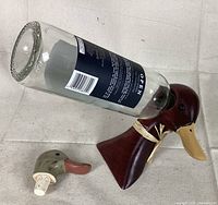 Wooden duck wine bottle holder shown holding a wine bottle with matching duck head stopper on a beige fabric background.