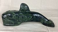 Side view of dark green/black killer whale sculpture showing detailed carving and traditional Indigenous design.