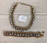 Full view of the Hattie Carnegie gold tone necklace and bracelet with aurora borealis rhinestones displayed on fabric.