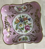 Top view of square pink porcelain Limoges bowl showing floral and gold decoration, scalloped edges.