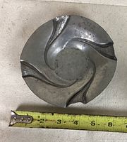 Top view showing the circular shape and swirled leaf designs of the pewter trinket bowl, with a measuring tape indicating about 5.5 inches diameter.