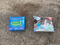 Two boxed unused inflatable pool toys shown side by side on pavement surface. One blue box labeled Swimline with a green fruit slice island lounger pictured, the other box labeled Banzai Hydro Disc Jam showing inflatable water game items and children playing in a pool.