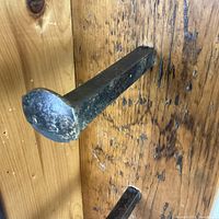 Close-up view of iron railway spike hook mounted on the wooden board showing wear and texture