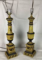 Front view of the pair of yellow tole painted lamps showing Civil War battle scenes on bases and columns under lamp fittings.