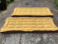 Two single-sized mustard yellow inflatable mattresses with tufted design laid out on pavement.