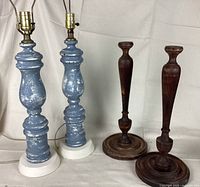 Two blue turned wooden lamp bases on white metal bases and two dark wooden candlestick bases against white backdrop.