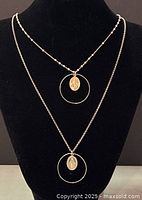 Two-strand necklace displayed on a black stand showing the silver chains and religious medal pendants inside circular hoops.