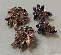 Two pairs of vintage rhinestone earrings, one with pink and olive marquise and round stones, the other with purple and pink stones in a floral shape.