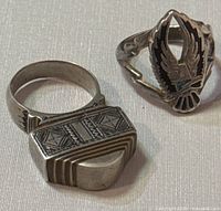Photo showing both vintage silver rings on a light surface, highlighting the geometric patterned ring and the eagle with lightning bolt ring