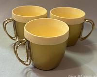 Three retro NFC insulated coffee mugs, beige upper rim and gold lower body with gold metallic handles, shown from the front.
