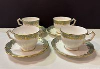 Four Aynsley bone china teacups with matching saucers, white with green and gold accents, arranged in pairs on a white surface.