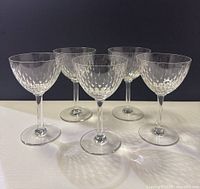 Five Baccarat crystal wine glasses arranged upright showing etched leaf pattern on bowls, slender stems, flat bases, against a dark background.