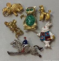 Six costume jewelry brooches arranged in two images showing animal and character motifs, including an armadillo, cat, poodle, mouse, horse and jockey, and a rabbit.