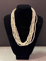 Front view of the 7-strand pearl necklace displayed on a black bust stand showing the layering and color of the pearls.