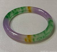 Top angle view of the multicolor jade bangle showing distinct color sections of green, lavender, and yellow, and the round smooth polished shape.