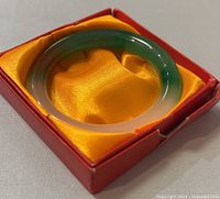 Natural Asian multicolor jade round-shaped bangle in original red box with yellow satin lining. The bangle has a smooth, polished finish with green, white, and brown color variations.
