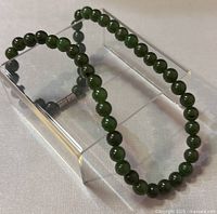 Photo of the natural nephrite jade bead necklace laid out showing the round beads and metal clasp detail.