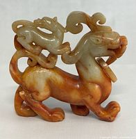Front angle view of the carved jade beast showing the detailed body, face, and smaller figure on its back, highlighting the jade coloration and the ring in the mouth.