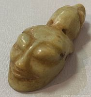 Front and top view showing carved human-like head details, smooth polished stone surface, minor discoloration spots.
