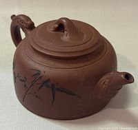 Side view of dark brown clay teapot with hand painted bamboo designs and sculpted animal head on handle and spout.