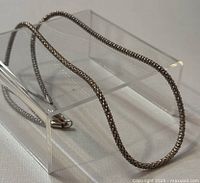 Close-up of silver chain necklace draped over a clear stand highlighting chain texture and length.