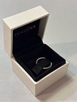 Pandora 925 silver ring placed inside black velvet interior of white textured jewelry box, lid open showing brand name inside.
