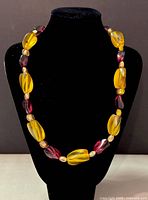 Front view of the retro necklace displayed on a black velvet stand showing the alternating amber yellow and burgundy beads separated by smaller pink beads.