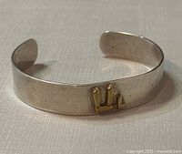 Open cuff sterling silver bracelet with a gold-tone decorative feature on front, showing minor surface wear.