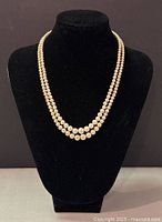 Photo showing the full necklace with two pearl strands displayed on a black bust stand.
