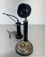 Full front view of the vintage candlestick telephone showing the black base with silver rotary dial and black earpiece hanging from hook.