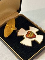 Front view of Maltese Cross medal showing white enamel cross with crowned red heart and gold-tone pin with star design, resting in original fitted display case with black velvet interior.