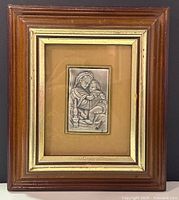 Full view of the framed silver icon showing the Virgin Mary holding baby Jesus on beige background and wooden frame with gold inner border.