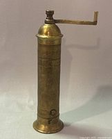 Front view showing the full hand-etched brass pepper mill with crank handle upright.