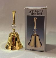 Gold plated table bell displayed next to its original box, showing the bell's design and packaging details.