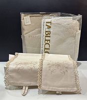 Image of embroidered napkins with crocheted edges and packaged cloth behind them.