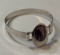 Close-up view of cuff bracelet showing front with purple oval gemstone centerpiece and silver band.