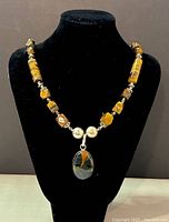 Front view of necklace on black bust showing tiger's eye beads and agate pendant