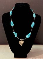 Necklace displayed on black bust showing turquoise beads and silver heart pendant.
