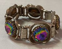 Side angled view of vintage bracelet showing textured silver-tone metal and vibrant, faceted multicolored rhinestones with gold-tone scalloped bezels.