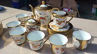 Overview of the porcelain tea set arranged on table, showing all cups, saucers, teapot, sugar bowl, and creamer with gold rims and dragon motifs.