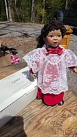 Front view of the porcelain doll showing facial details, white lace blouse with red bow, and red skirt.