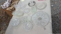 Multiple assorted cut crystal glassware pieces arranged on outdoor surface including divided tray, bowls, plates and serving dishes.