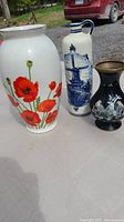 Three ceramic vases outdoors on table: white floral vase, tall cream windmill vase, small black decorative vase