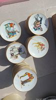 Several stacks of small porcelain plates featuring colorful Norman Rockwell illustrations representing the four seasons on a light surface.