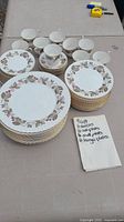 Photo showing full set of stacked plates, cups, and saucers with handwritten list of included pieces.